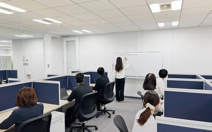 ホワイドボードに書き込んでいる女性社員とそれを見ている社員たち